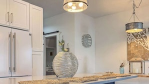A modern kitchen with white cabinets, a blue island with bar stools, and pendant lighting. - Amenities in this walk to Beach, New 3bed/3.5bath (Cape Charles)