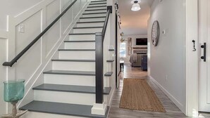 A modern staircase with a glass railing, a wooden floor, and a hallway leading to a kitchen area. - Amenities in this walk to Beach, New 3bed/3.5bath (Cape Charles)