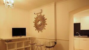 Ein Wohnzimmer mit Fernseher, einem Spiegel in Sonnenstrahlform und zwei Barhocker.