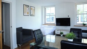 A modern hotel room with a bed, a TV, a glass table, and two black chairs.