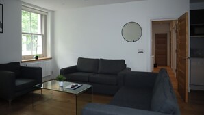 A modern living room with a sofa, a glass coffee table, and a potted plant.