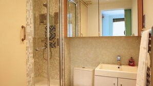 A bathroom with a glass-enclosed shower, a toilet, and a sink with a mirror above.