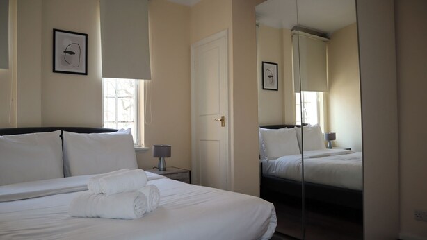 Habitación de hotel con una cama grande, una mesita de noche con lámpara, una puerta y un espejo.