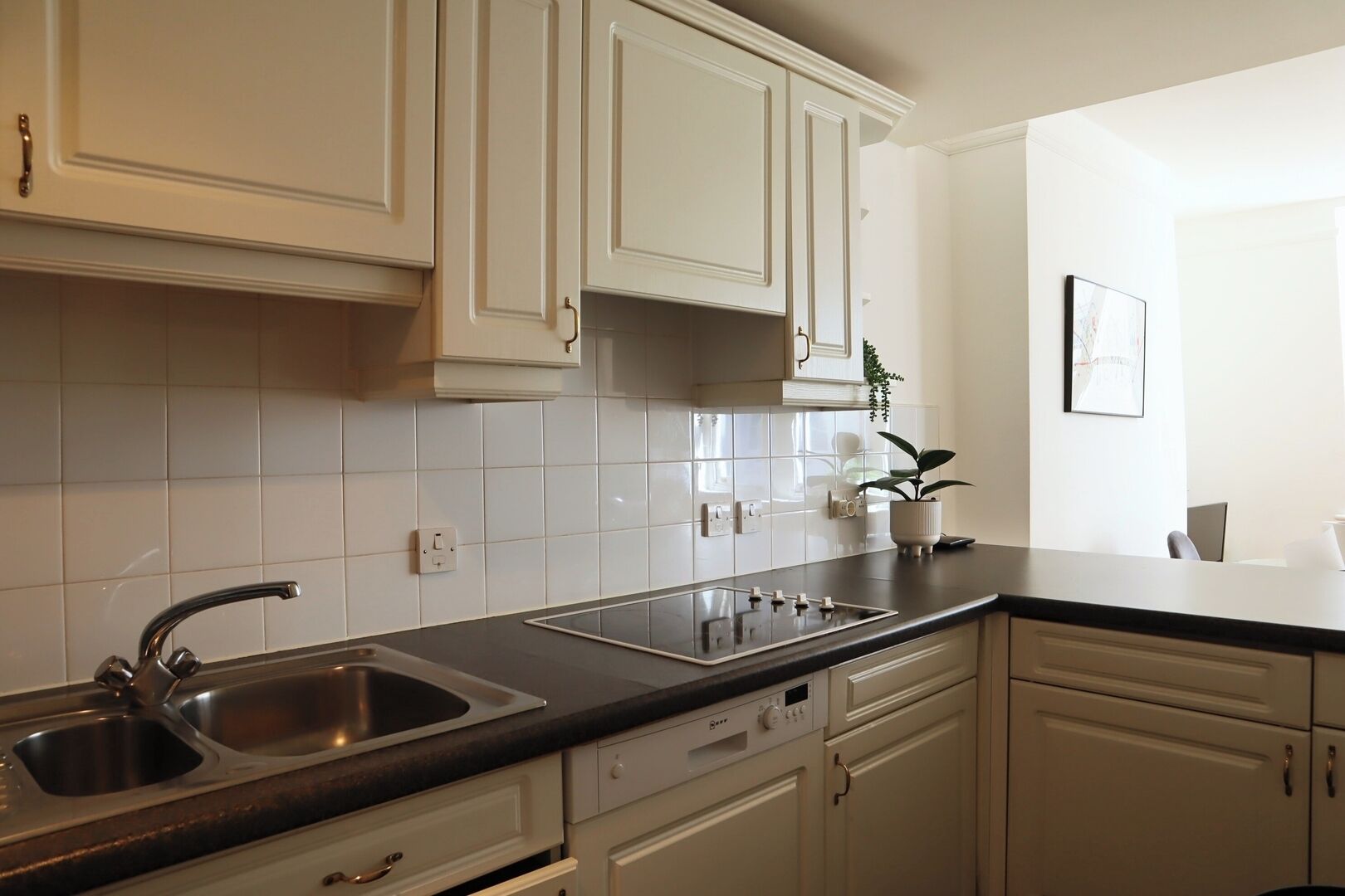 A modern kitchen with white cabinetry, a black countertop, a stainless steel sink, and a built-in oven.