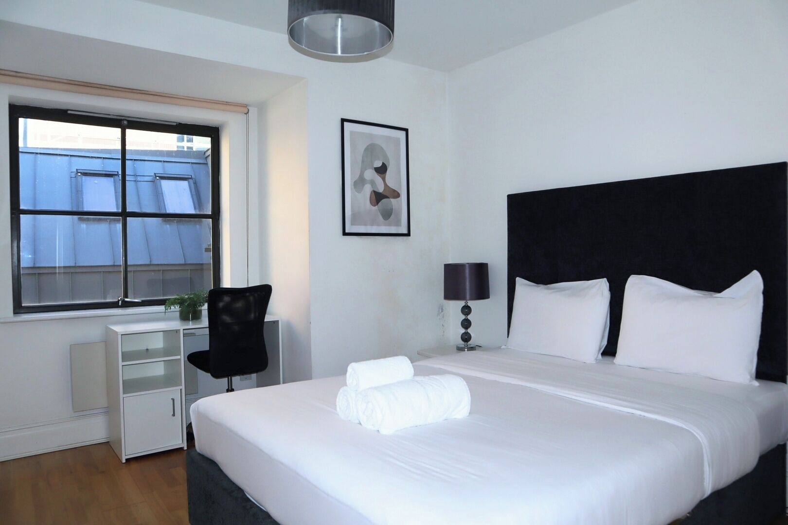 Une chambre d’hôtel avec un grand lit, un bureau, une chaise, une fenêtre et un tableau encadré au mur.