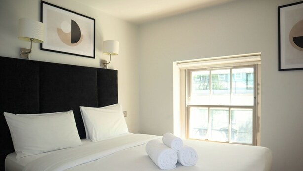Hotelkamer met een groot bed, twee bedlampen, een raam met uitzicht en een gekaderd kunstwerk boven het bed.