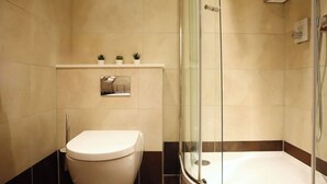 Een badkamer met toilet, een douche met glazen wanden en een plankje met kleine planten.