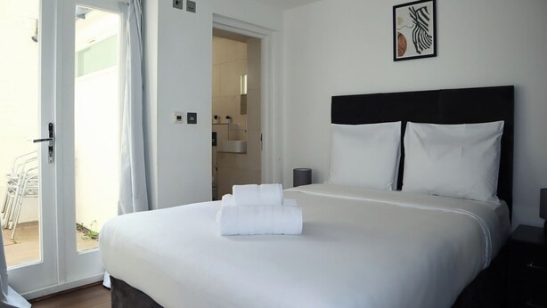 Habitación de hotel con cama, mesita de noche, una obra de arte enmarcada y un baño visible a través de una puerta abierta.
