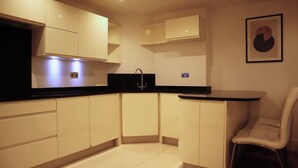 Una cocina compacta con armarios blancos, una encimera negra y un pequeño comedor con una silla.