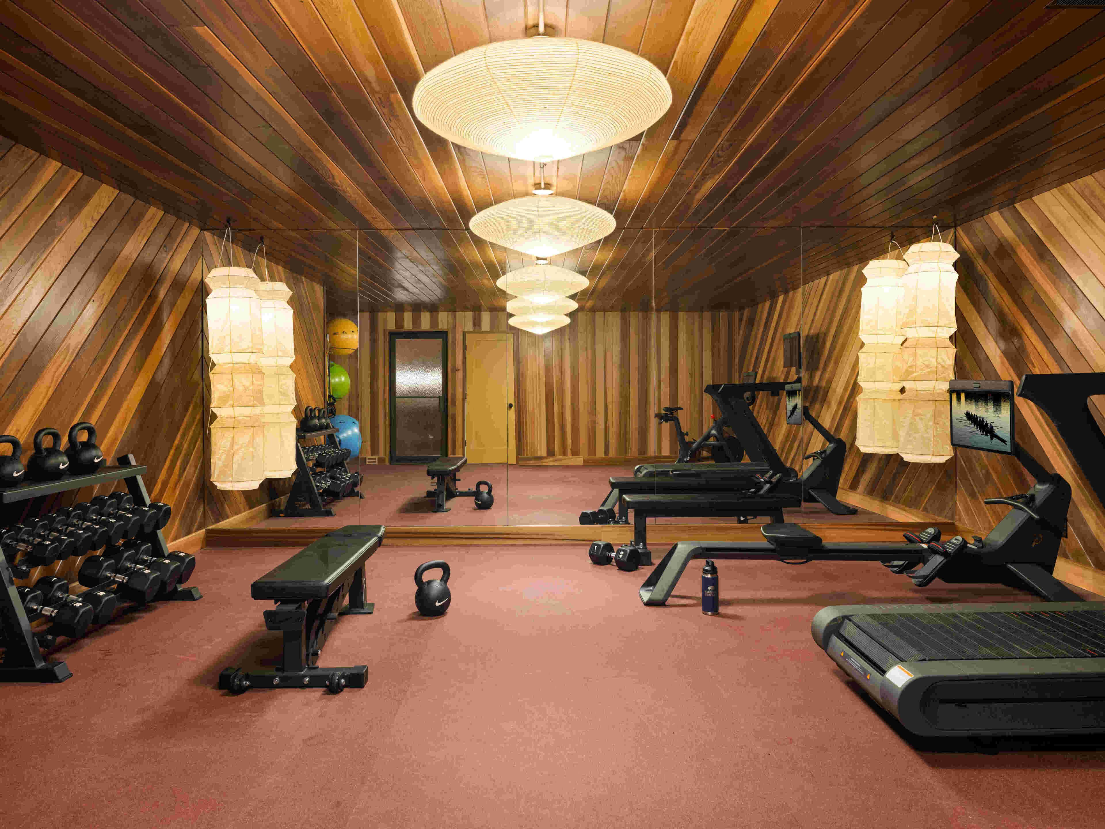Un gimnasio con equipo de ejercicio, una banca, pesas de mancuerna y un espejo.