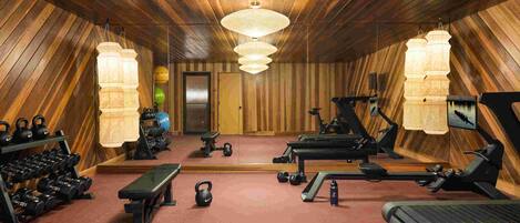 Un gimnasio con equipo de ejercicio, una banca, pesas de mancuerna y un espejo.