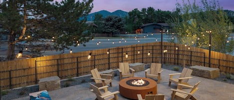 An outdoor seating area with a fire pit, wooden chairs, and a stone floor.