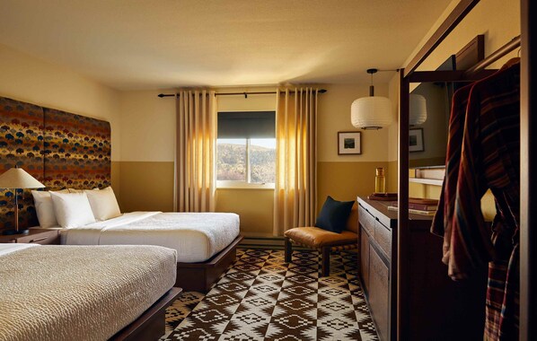 A hotel room with two beds, a chair, a mirror, and a window with curtains. - Wandering Buffalo (Bozeman)