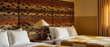 Una habitación de hotel con dos camas, un cabecero estampado, una mesita de noche con lámpara y una ventana con cortinas.