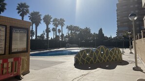 A pool area with palm trees, a building with a sign, and a patterned structure.