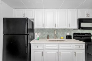 A kitchen with white cabinets, a black refrigerator, a microwave, and a stove.