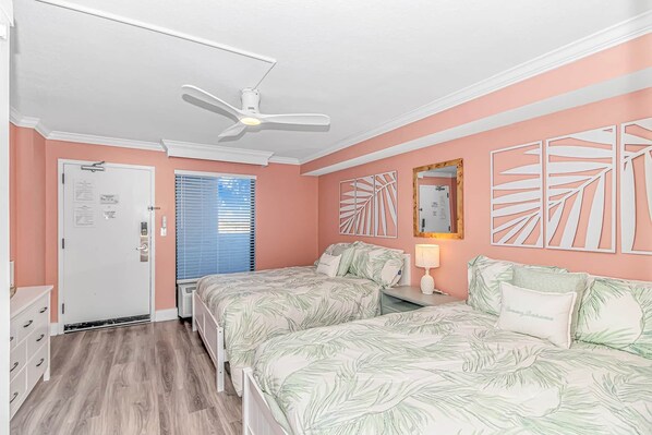 A bedroom with two beds, a ceiling fan, a door with a bulletin board, and a window with blinds.