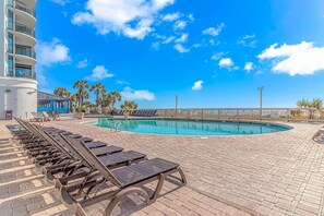 A pool area with lounge chairs, a clear sky, and palm trees. - Oceanfront Luxe 1BR w/ Pools & Waterpark! (Myrtle Beach)