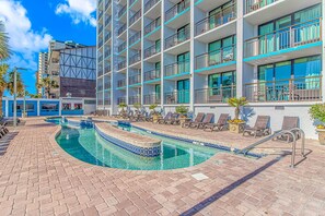 A hotel with a swimming pool, sun loungers, and a view of the surrounding buildings.