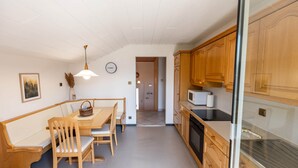 A kitchen with wooden cabinets, a microwave, and a dining area with a table and chairs. - Apartment Rosengarten (Tiers)