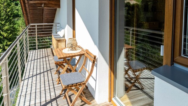A wooden balcony with a table and chairs, a view of the surrounding landscape, and a large window. - Apartment Rosengarten (Tiers)