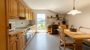A kitchen with wooden cabinets, a dining table, and a view through a door to the outdoors. - Apartment Rosengarten (Tiers)