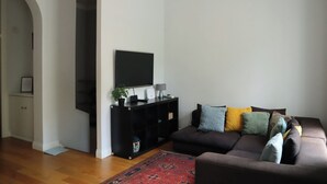 Een woonkamer met een donkerbruine bank, een zwarte tv-meubel, een flatscreen televisie en een rood tapijt met dessin.