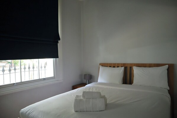 Habitación de hotel con cama, mesita de noche, lámpara y ventana con vista a una valla.