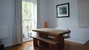 Een kamer met een houten tafel, een bank, een raam met gordijnen en een lijst met een afbeelding aan de muur.