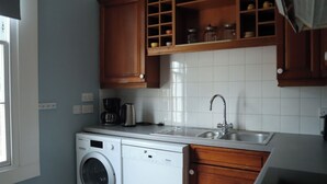 Een kleine keuken met een wasmachine, een koffiezetapparaat en een spoelbak.