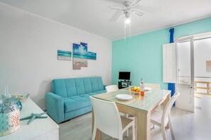 Een moderne woonkamer met een turquoise bank, een glazen eettafel en een plafondventilator.