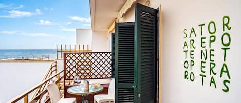 A balcony with a table and chairs, a view of the sea, and a wall with green text.