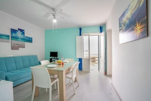 Un salon moderne avec un mur d’accent de couleur turquoise, un canapé blanc, une table à manger en verre et un ventilateur de plafond.
