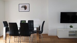 A modern living room with a dining area, a flat-screen TV, and a minimalist decor.