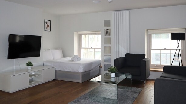 A modern, well-lit living room with a bed, a TV, a sofa, and a coffee table.