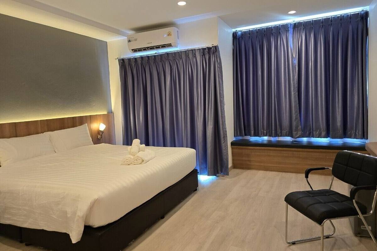 A hotel room with a large bed, a bedside table with a lamp, a window with curtains, and a chair.