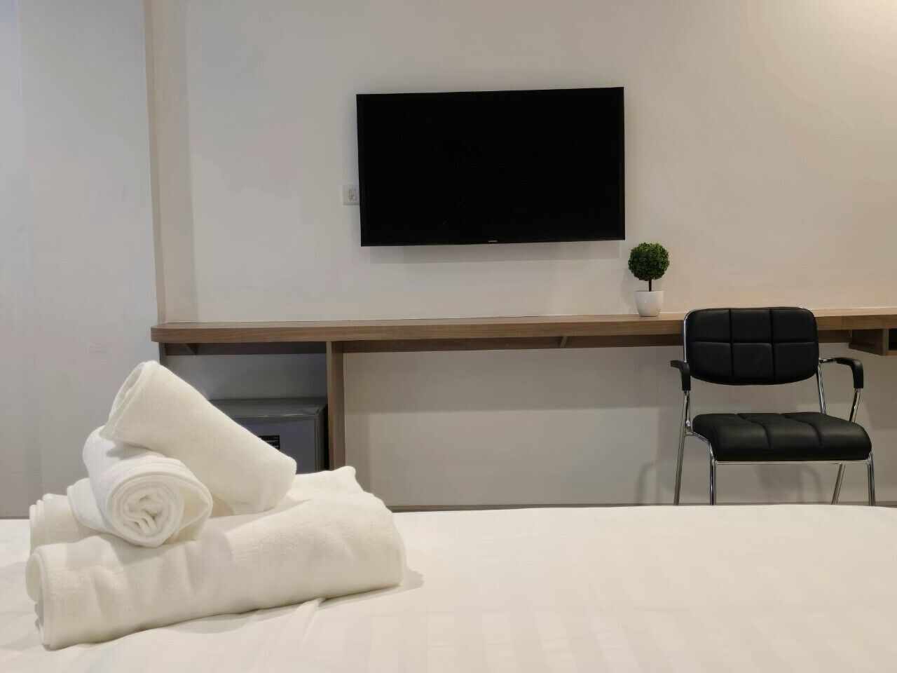 Une chambre d’hôtel comprenant un lit, un téléviseur à écran plat fixé au mur, un bureau avec une chaise et une petite plante en pot.