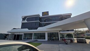 A modern building with a prominent logo on the facade, large windows, and a parking area with a car and a motorcycle.
