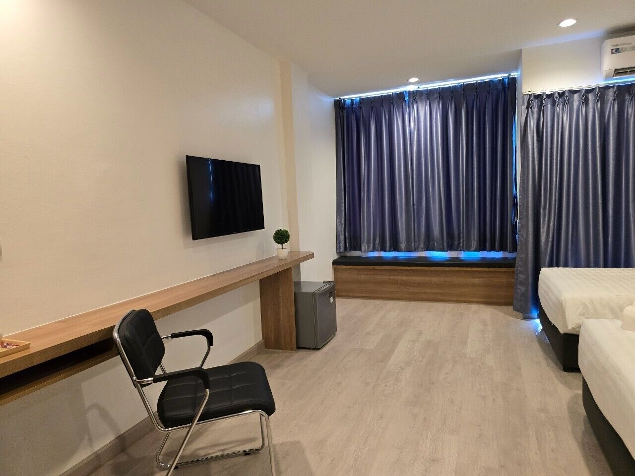 Ein Hotelzimmer mit Bett, Schreibtisch mit Stuhl, Wandfernseher und einem Fenster mit Vorhängen.