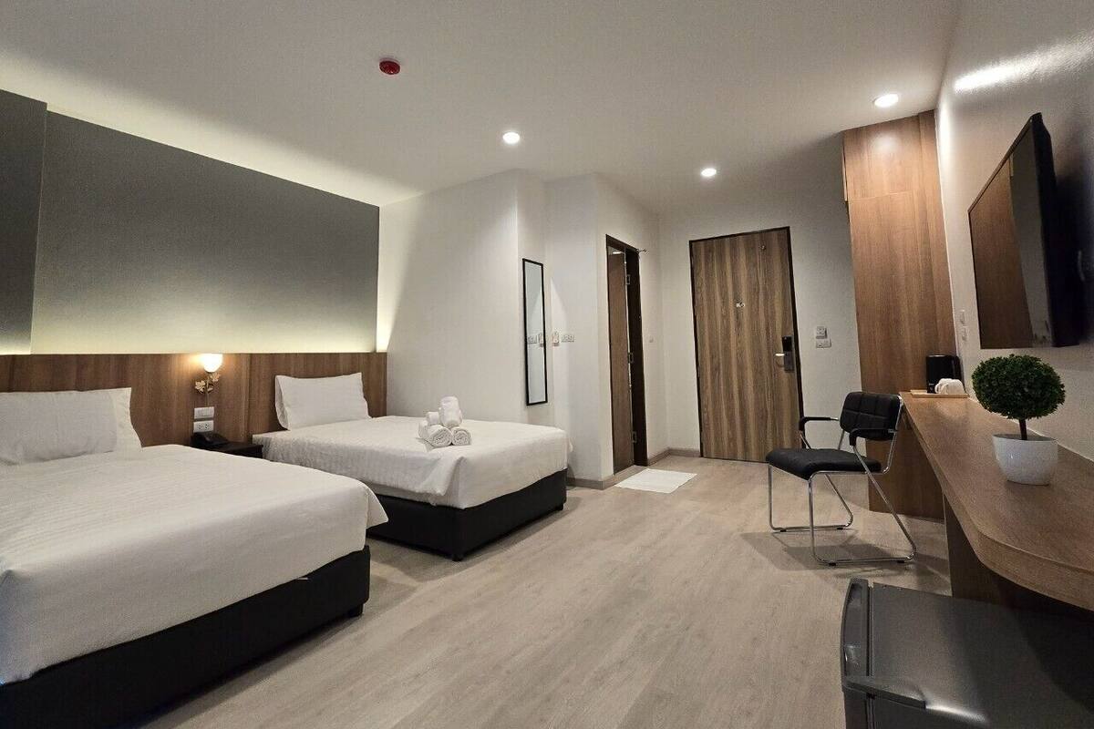 A modern hotel room with two beds, a desk, a chair, and a small potted plant.