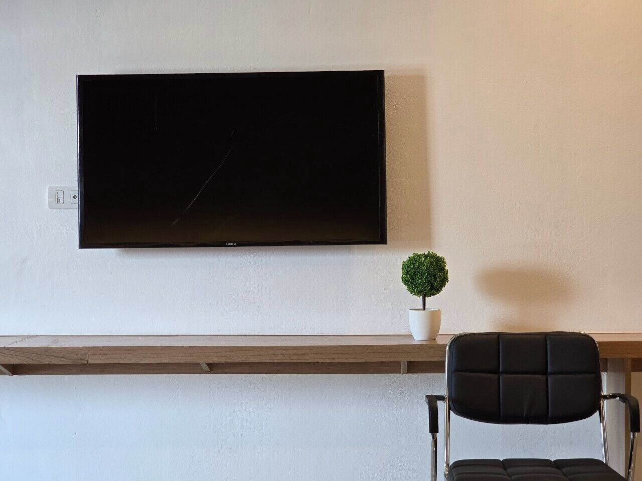 Una sala de estar moderna con un televisor de pantalla plana montado en la pared, una planta pequeña en maceta y un sillón negro con respaldo acolchado.
