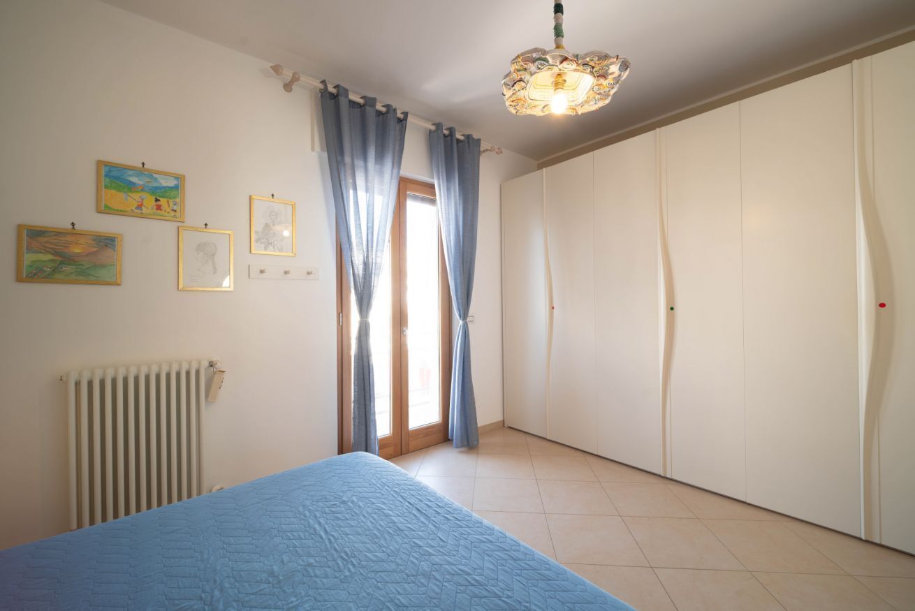 A bedroom with a bed, a radiator, a door, and a window with curtains.