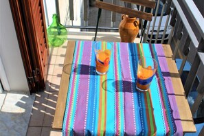 A balcony with a table covered by a colorful striped tablecloth, two glasses of orange beverage, a green bottle, and a clay pot. - WePuglia - La Perla Bianca (Polignano a Mare)