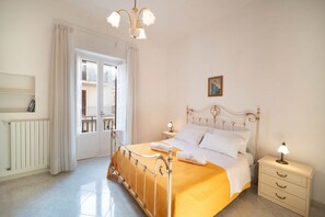 A bedroom with a bed, bedside table, nightstand, and a window with curtains. - WePuglia - La Perla Bianca (Polignano a Mare)