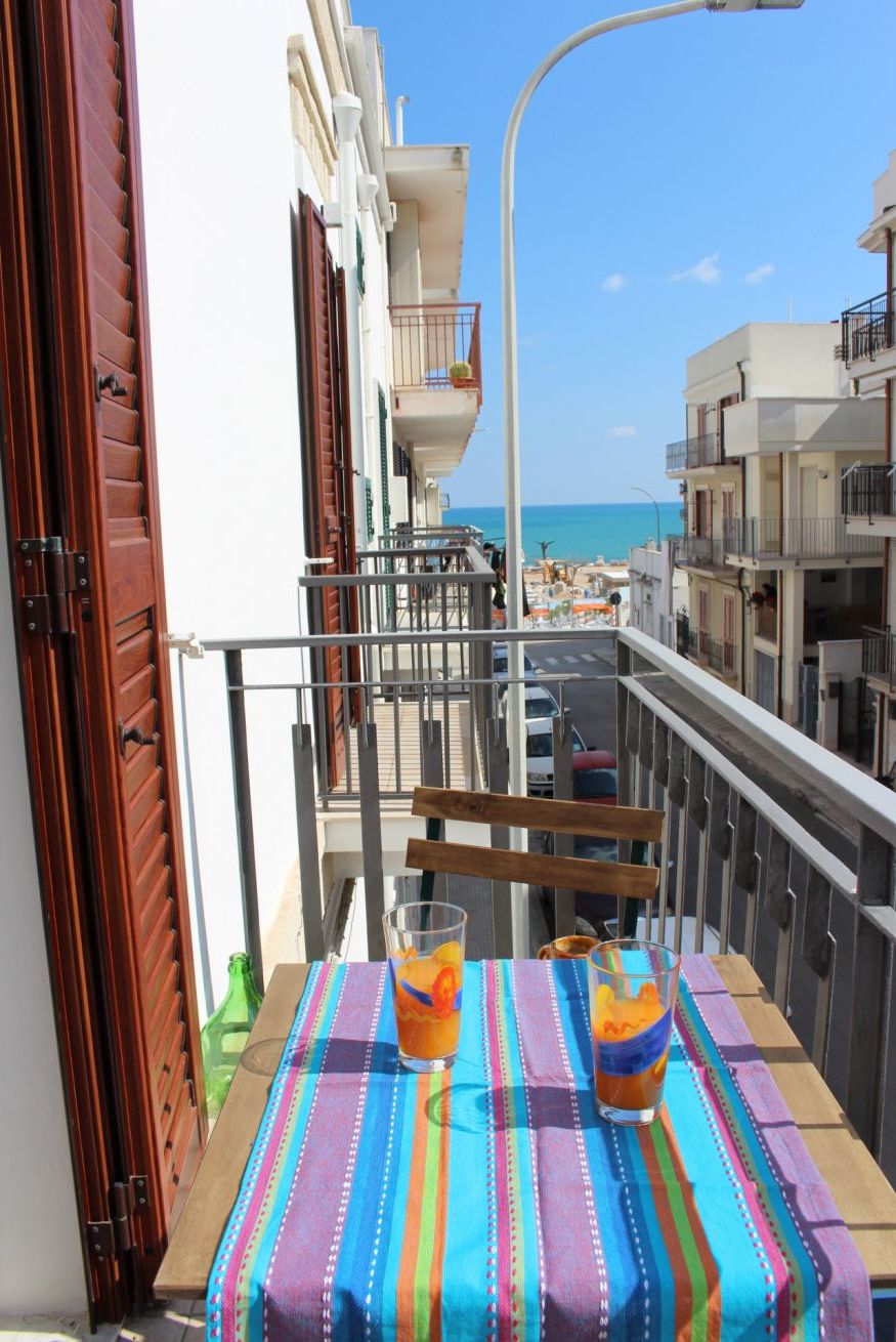 Varanda com mesa posta para dois, vista para a rua e para o mar.