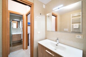 A modern bathroom with a large mirror, a white sink, and wooden cabinetry. - WePuglia - La Perla Bianca (Polignano a Mare)