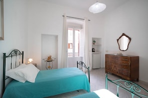 A bedroom with a bed, a dresser, a mirror, a nightstand, and a window with curtains. - WePuglia - La Perla Bianca (Polignano a Mare)