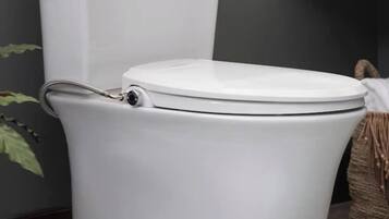 Des toilettes blanches, avec un abattant et une poignée pour tirer la chasse d’eau.