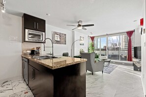 A modern kitchen with a built-in microwave, a large island with a sink, and a ceiling fan. - BC Place & Rogers Arena Central, Modern w/ AC (Vancouver)