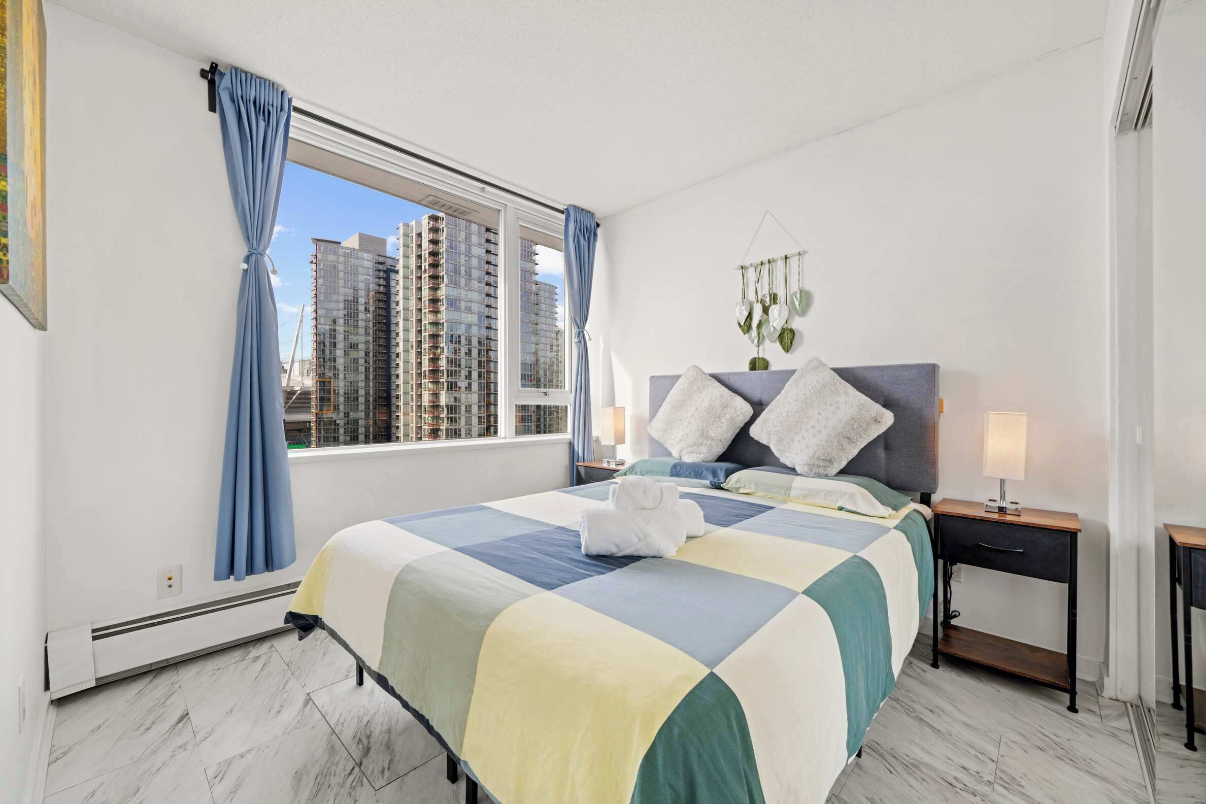 Hotelkamer met een groot bed, nachtkastje, hangplant en uitzicht op hoge gebouwen.
